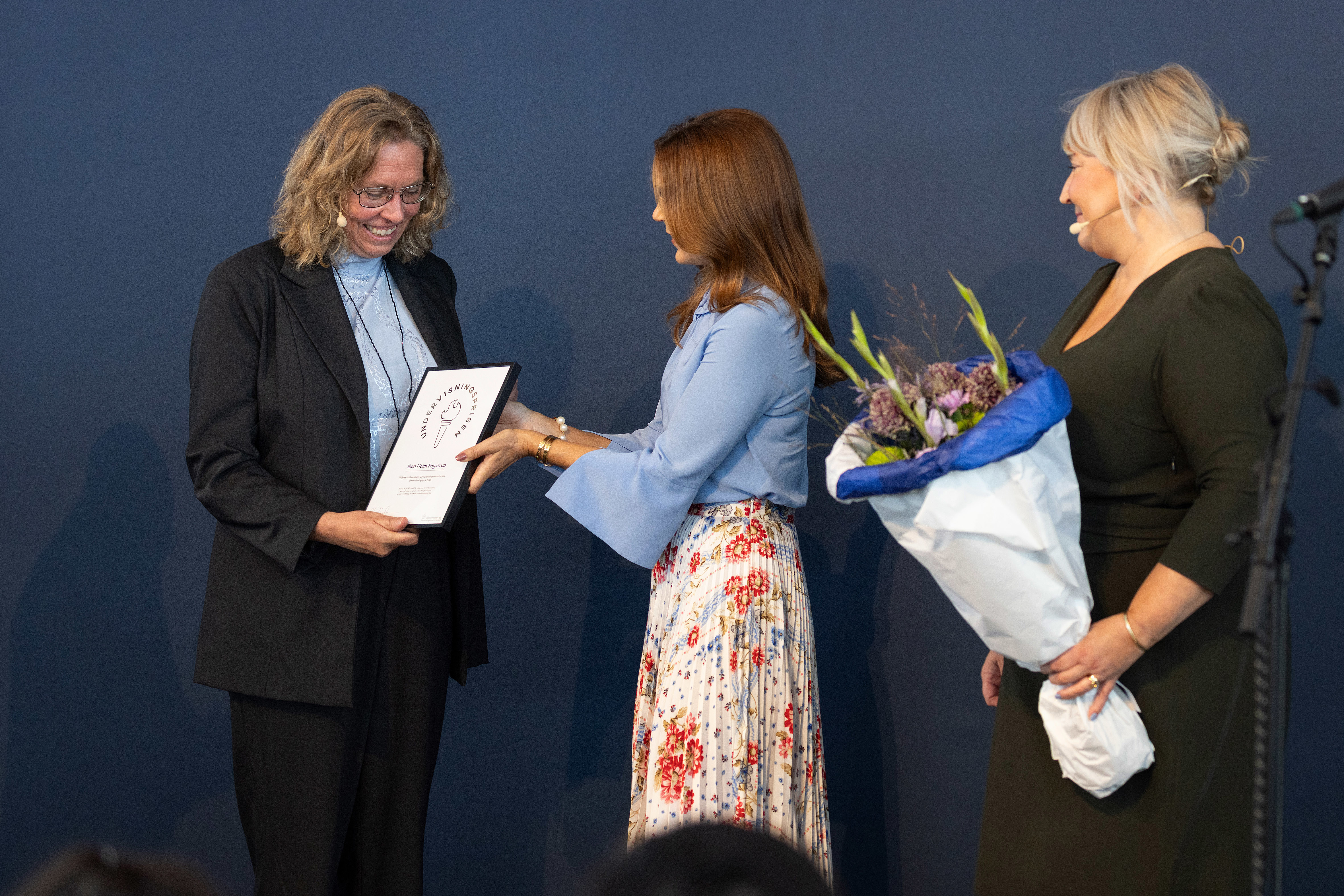 Iben Holm Fogstrup, vinder af Undervisningsprisen 2024 får overrakt diplom og blomster af H. M. Dronningen og uddannelses- og forskningsminister Christina Egelund.
